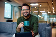 © Drazen - Happy entrepreneur drinks coffee while using digital tablet in office and looking at camera.