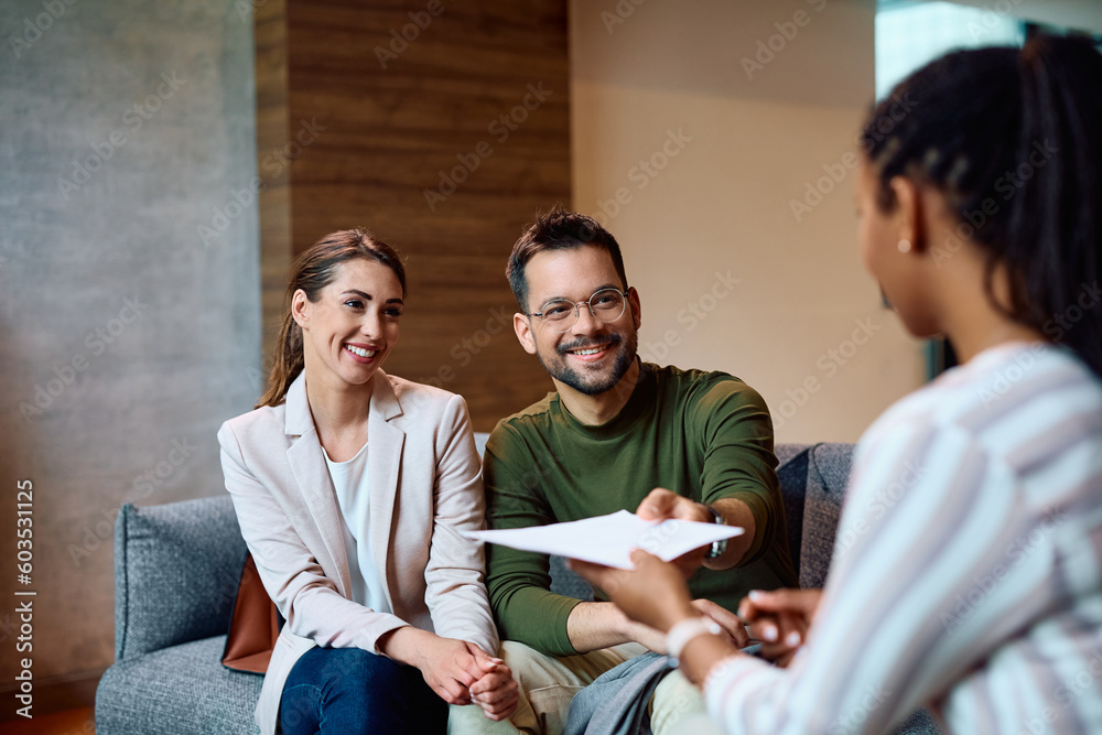 Happy couple giving documents to their bank manager during meeting in office.