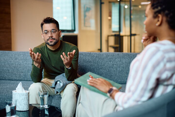 Young man talks during session with mental health therapist in office.