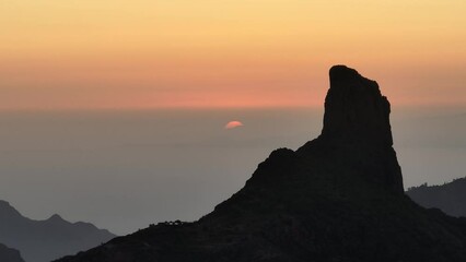 Wall Mural - Aerial video of sunset behind Roque Bentayga on Gran Canaria with orange sky and silhouettes of Tenerife and La Gomera