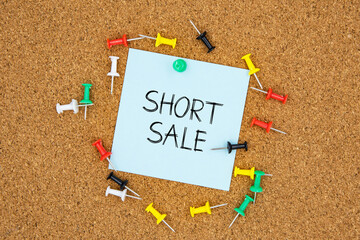 Poster - Short sale text on light blue post-it paper pinned on bulletin cork board surrounding by multi color pins. This message can be used in business concept about short sale.