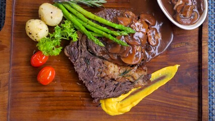 Wall Mural - Close-up of juicy beef steak with grilled vegetables on a wooden board. Slow motion of cutting tenderloin steak by knife and picked up by a fork. Top view of lunch food