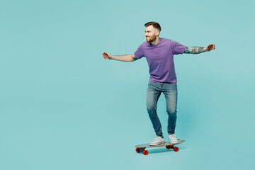 Full body side profile view young man wear purple t-shirt riding skateboard pennyboard with outstretched hands isolated on plain pastel light blue cyan background studio portrait. Lifestyle concept.