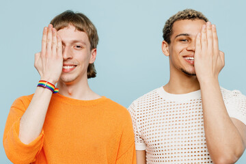 Wall Mural - Young happy couple two gay men wear casual clothes together cover half on face with hand isolated on pastel plain light blue color background studio portrait. Pride day june month love LGBTQ concept.