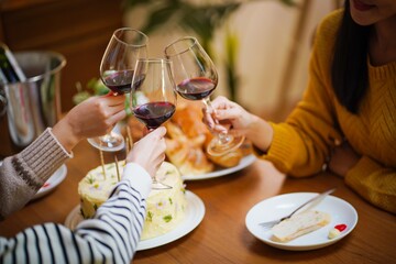 Cheerful friends enjoying home Birthday holiday party. Asian Friends cheering drinking red wine celebrating Christmas or New Year party