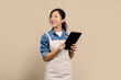 © PBXStudio - Beautiful asian waitress wearing brown apron work in coffee shop holding digital tablet and looking at copy space isolated on light brown background. Small business startup concept
