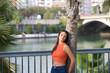© @skuder_photographer - Young and beautiful woman leaning on the trunk of a palm tree. Woman is happy and relaxed and enjoying the sunny day in seville, spain. The woman is wearing jeans and orange top.