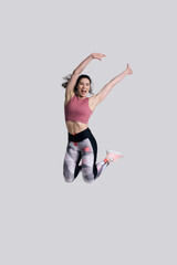 Determined strong young sportswoman, smiling and raising arm while jumping high on white background.