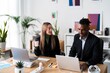 © Studio Marmellata - Positive multiethnic coworkers in formal clothes sitting at wooden table with laptops and cups of takeaway coffee while working on business project together in modern office