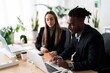 © Studio Marmellata - Positive multiethnic coworkers in formal clothes sitting at wooden table with laptops while working on business project together in modern office