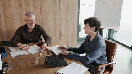 Wall Mural - Elderly man and woman leaders discuss work tasks at desk in office