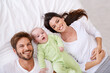© Marius Venter/peopleimages.com - Top view, portrait and happy parents with baby on bed for love, care and quality time together at home. Smile of mother, father and family with cute newborn kid relaxing in bedroom, fun and happiness