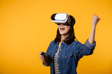 Poster - Young asian woman happy success wearing virtual reality headset game entertainment and holding joystick controller isolated on yellow background. Winner of cyber future video game concept.