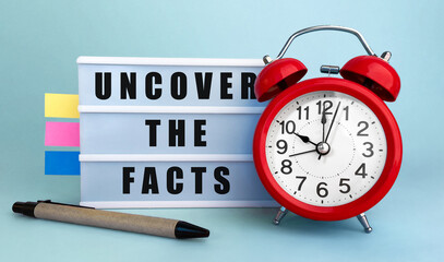 Poster - text uncover the facts written on the lightbox with alarm clock and colorfull stickers on blue backg