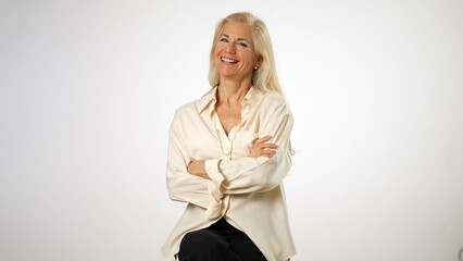 Portrait of elegant mature elderly woman wearing pearl necklace sitting on stool smiling, with copy space. Business woman emotions