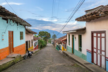 Streets Of A Town In Colombia, Where You Can See People Walking Through Colored Houses. Town In The Mountains Of Latin America.