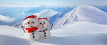 Christmas Winter Banner With Couple Of Snowmen In A Santa Hats On Their Heads Against The Backdrop Of Snowy Mountains. Holiday Background With Copy Space For Text