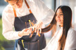 © chokniti - Beautiful woman has a haircut at a professional hairdresser salon barber uses scissors to trim her hair with a coiffure hairstyle, The lady with long hair smiling and happy with her hairstylist.