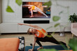 © Clique Images - Modern Caucasian woman having yoga workout at home doing stretching and balancing asana with fitness trainer on TV screen