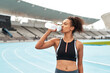 © Emil Lime/peopleimages.com - Fitness, running and woman on track drinking from bottle at stadium, relax during marathon training or exercise. Workout time, health and wellness, healthy female sports runner at area with water.