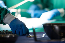 Gloved Hand Of Surgeon Picking Up Surgical Tool During Operation On Patient In Operating Theatre
