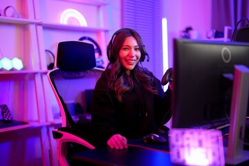 Wall Mural - Asian pretty streamer girl smile and hold controller for game battle play while sitting comfort ergonomic chair with neon sign background in entertainment gamer room