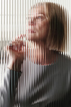 Vertical Through Textured Glass Wall Portrait Of Modern Mature Caucasian Woman With Blond Bob Cut Hair Thinking Of Something, Striped Distortion Effect