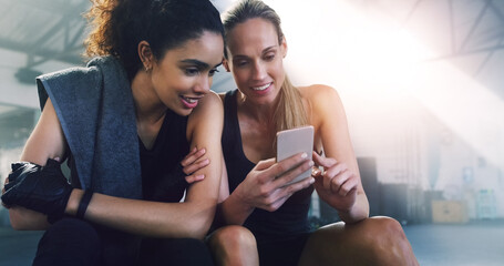 Canvas Print - Fitness, phone and girl friends watching a video in a gym with women and smile from training. Social media app, mobile and female person in wellness, exercise and workout class taking a break