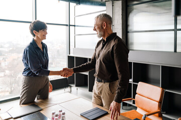Professional mature smiling colleagues finished business meeting and shaking hands in office