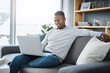 © Angelo J/peopleimages.com - Black man relax on couch with laptop, streaming online in living room and subscription service with internet. Technology, connectivity and happy male person chill at home watching tv show or film