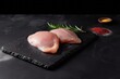 Raw chicken breast on a black board with rosemary on the side. Generative AI
