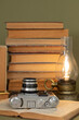 Old books, an analog camera and a stylized lamp on an olive green background.