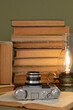 Old books, an analog camera and a stylized lamp on an olive green background.