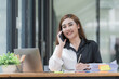 © Songsak C - Happy young Asian businesswoman talking on the mobile phone and smiling while sitting at her working place in the office.