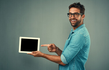 Poster - Happy man, tablet and pointing to mockup screen for advertising against a grey studio background. Portrait of male person smiling showing technology display, chromakey or copy space for advertisement