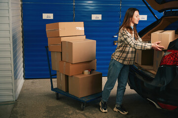 Wall Mural - Full length of lady with cardboard boxes near trunk of the car into warehouse