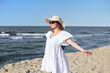© rogerphoto - Happy blonde woman is on the ocean beach in a white dress and sunglasses, open arms.