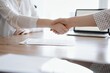 © rogerphoto - Business people shaking hands above contract papers just signed on the wooden table, close up. Lawyers at meeting. Teamwork, partnership, success concept.