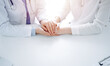 © rogerphoto - Doctor and patient sitting near each other at the table in clinic office. The focus is on female physician's hands reassuring woman, only hands, close up. Medicine concept.