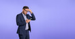 Worried male business executive touching head in stress and checking project deadlines on smart phone. Disappointed young manager reading recession news on cellphone isolated against blue background