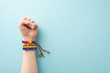 canvas print picture - A raised hand wearing a rainbow-colored wristlets with a clenched fist symbolizing strength and the fight for rights takes center stage in this photo on pastel blue backdrop with space for text or ad