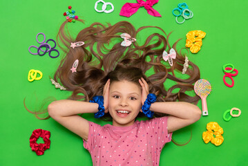 Accessories for children's hairstyles. A teenage girl with loose curly hair. A charming little girl with elastic bands and hair clips lies on a green isolated background.