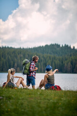 Wall Mural - Friends with backpacks look at beautiful lake at hiking