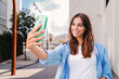 Happy young teenage female looking at camera and taking a selfie on smartphone showing a toothy smile. Portrait of laughing woman shooting a photo or record video with cellphone for social media. High