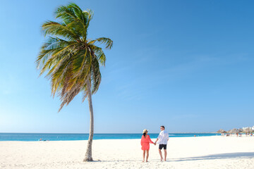 Wall Mural - Palm Beach Aruba Caribbean, a couple of men and women at a white long sandy beach with palm trees at Aruba Antilles.