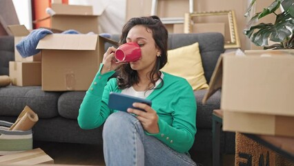 Sticker - Young beautiful hispanic woman watching video on smartphone drinking coffee at new home