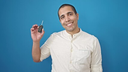 Poster - Young hispanic man holding key of new car over isolated blue background