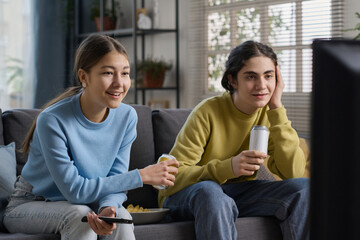 Wall Mural - Brother and sister drinking beverages and watching TV together while sitting on sofa in the living room