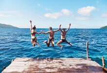 Water, Back Of People Jumping Off A Pier Holding Hands And Into The Ocean Together In Blue Sky. Summer Vacation Or Holiday Break, Freedom Or Travel And Young Group Of Friends Diving Into The Lake
