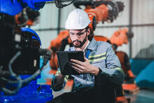 Factory Engineer Inspecting On Machine With Smart Tablet. Worker Works At Heavy Machine Robot Arm. The Welding Machine With A Remote System In An Industrial Factory. Artificial Intelligence Concept.